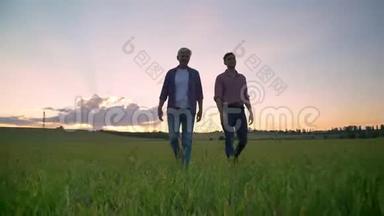 <strong>老爸</strong>爸和他成年的英俊的儿子一起散步，微笑着说话，背景是日落的麦田或麦田